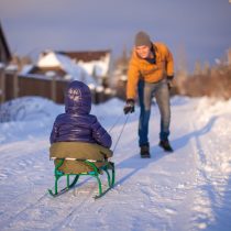 Young father sledding his little daughter on a sled in the snow outdoors